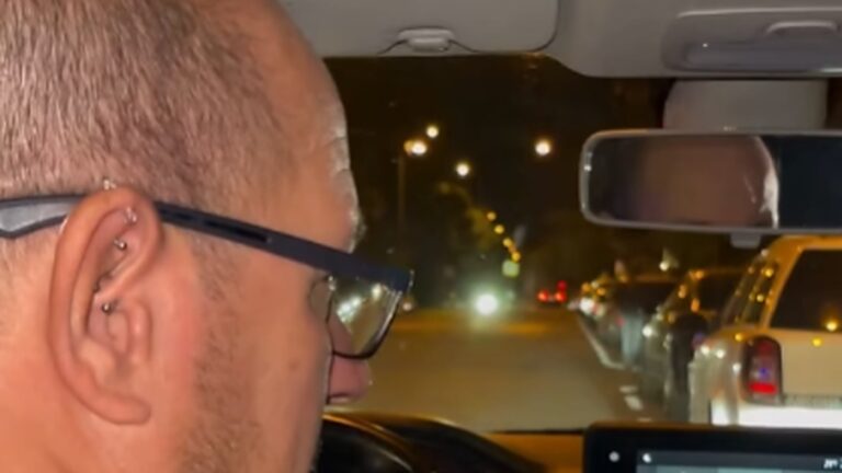 Kerületi rendész vezeti a járőrautót éjszaka egy józsefvárosi utcán, a szélvédőn át az utcai lámpák látszanak