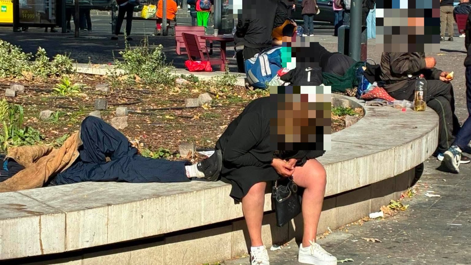 Emberek ülnek és fekszenek a Blaha Lujza tér egyik ülőfalán és virágágyásában