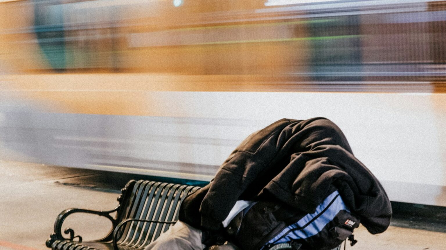 Egy ember alszik egy fém padon a városi utcán