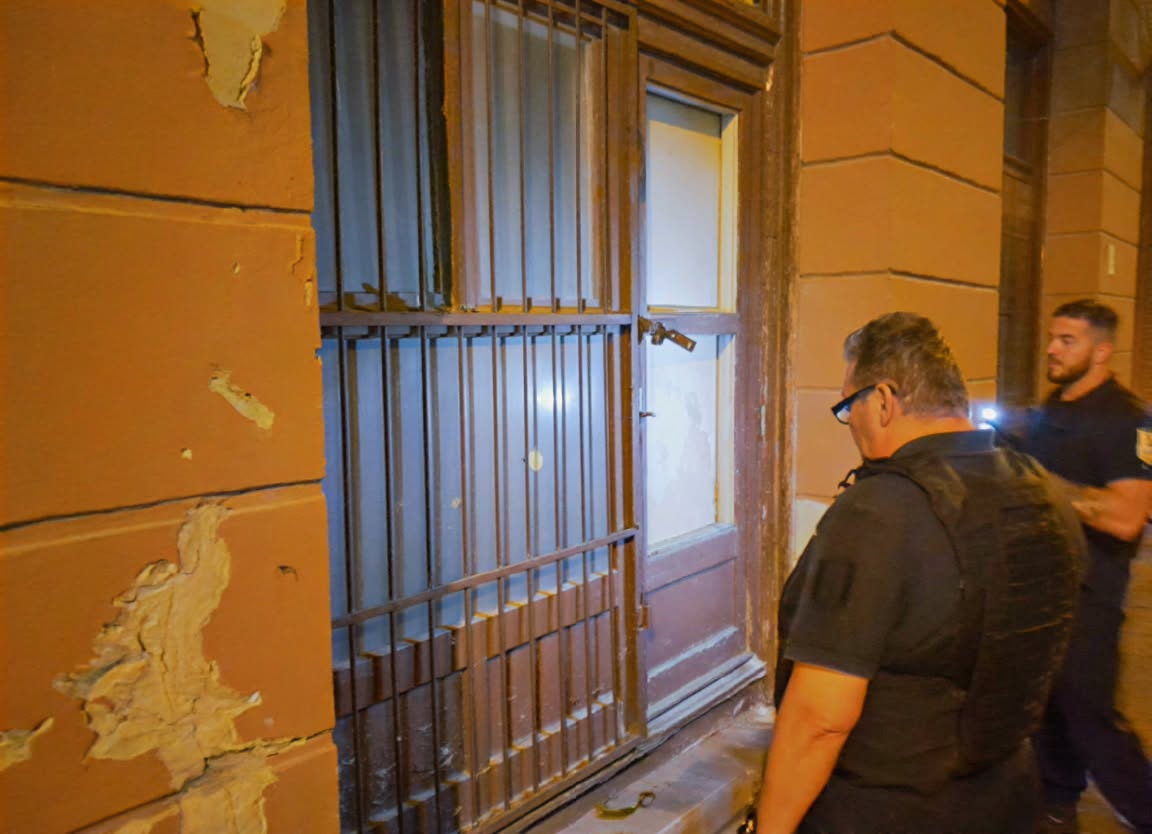 Két józsefvárosi rendész este zseblámpával egy önkormányzati ingatlan rácsos bejárati ajtaja előtt