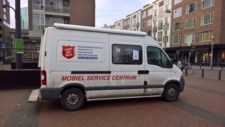 Az Üdvhadsereg fehér, mozgó segítőautója egy rotterdami belvárosi utcán
