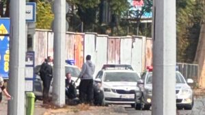 Rendőrautók és intézkedő rendőrök egy kelenföldi utcán, a járdán egy földön ülő férfi mellett
